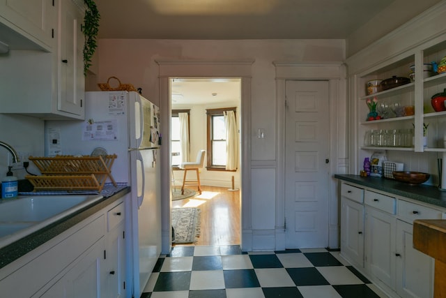 kitchen with dark countertops, freestanding refrigerator, tile patterned floors, white cabinetry, and a sink