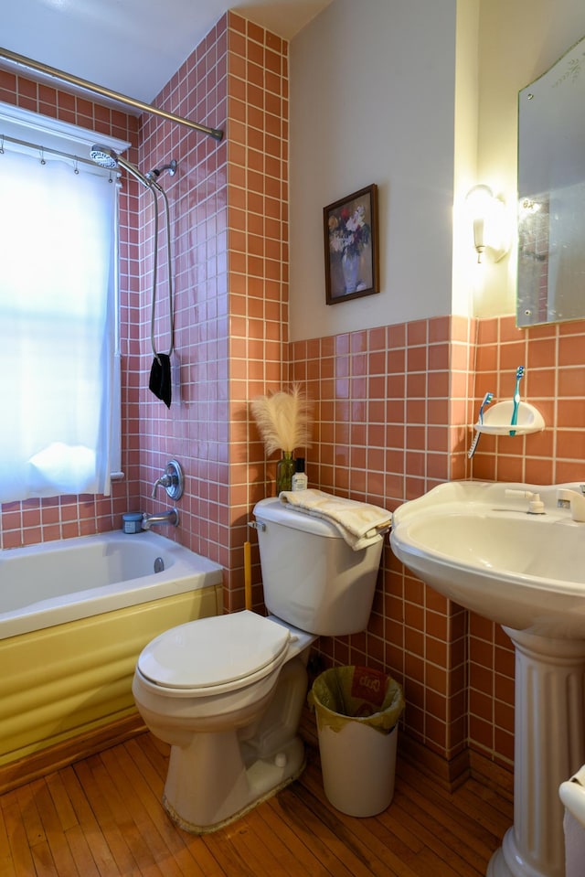 bathroom with hardwood / wood-style floors, wainscoting, shower / washtub combination, tile walls, and toilet