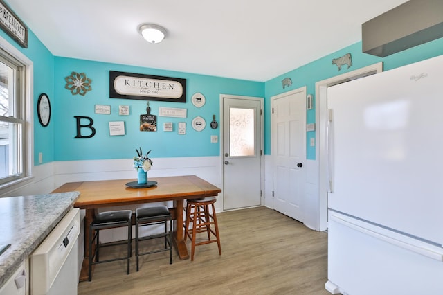 dining space featuring light wood-style floors, a healthy amount of sunlight, and a wainscoted wall