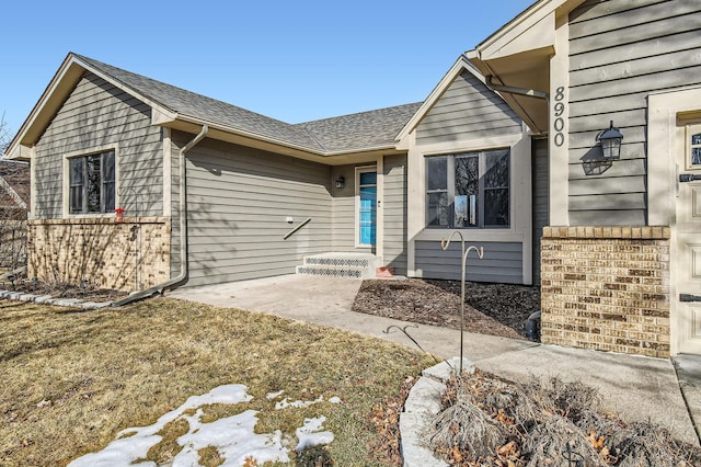 view of front of home featuring brick siding and roof with shingles