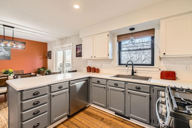 kitchen with gray cabinetry, light wood-style flooring, a sink, stainless steel appliances, and a peninsula