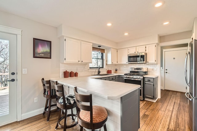 kitchen featuring tasteful backsplash, a peninsula, light wood-style floors, stainless steel appliances, and a sink