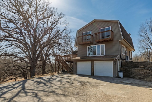 view of home's exterior featuring a gambrel roof, aphalt driveway, an attached garage, a balcony, and stairs