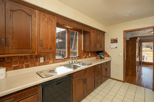 kitchen with light countertops, black dishwasher, decorative backsplash, light tile patterned flooring, and a sink