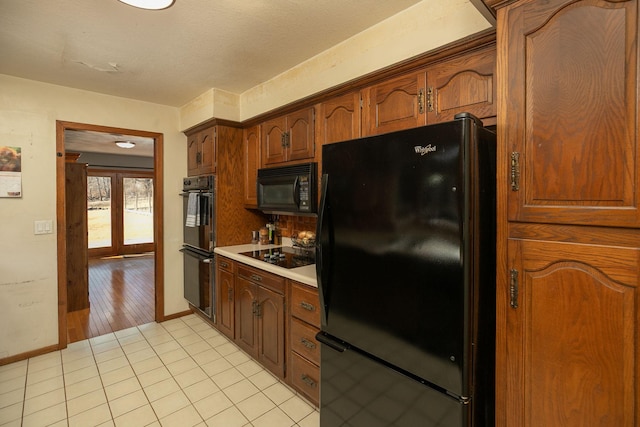 kitchen featuring brown cabinets, black appliances, light countertops, light tile patterned floors, and baseboards