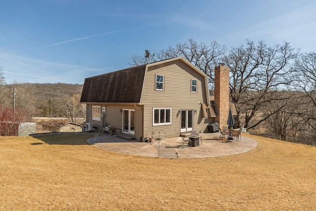 rear view of house with a patio, a yard, a gambrel roof, a chimney, and a shingled roof