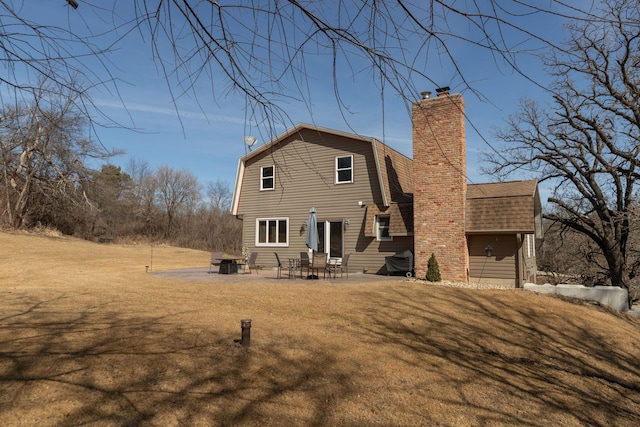 rear view of house with a gambrel roof, roof with shingles, a lawn, a chimney, and a patio