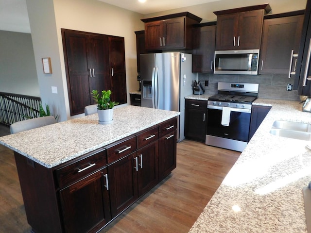 kitchen with dark brown cabinets, backsplash, a kitchen island, appliances with stainless steel finishes, and light wood-style floors