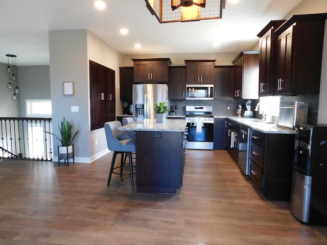 kitchen with a breakfast bar area, light stone counters, stainless steel appliances, dark brown cabinets, and a center island