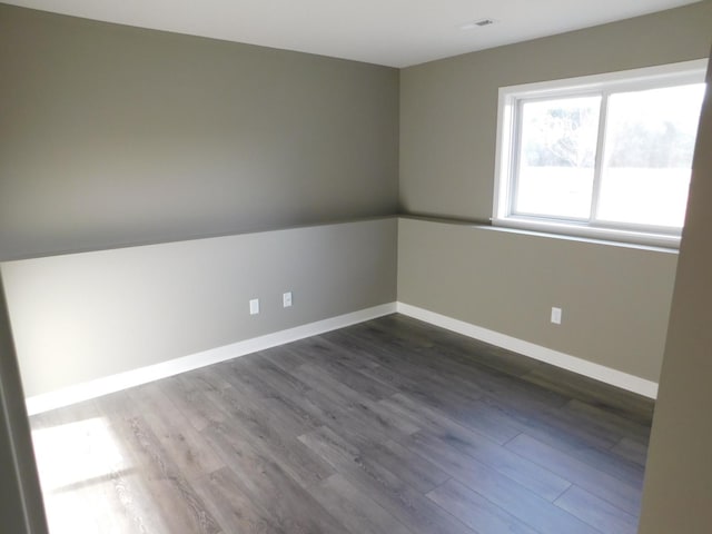 empty room featuring visible vents, baseboards, and dark wood-style flooring