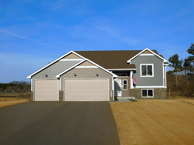 tri-level home with aphalt driveway, an attached garage, and stone siding