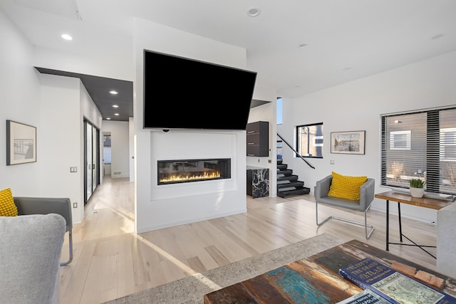 living room with recessed lighting, light wood-type flooring, a glass covered fireplace, and stairway