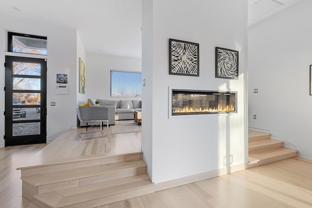 foyer entrance with stairway, a glass covered fireplace, and wood finished floors