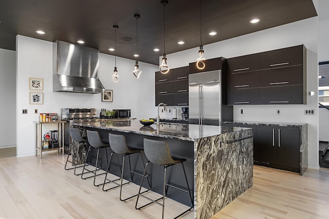 kitchen with wall chimney range hood, a breakfast bar, light wood-type flooring, stainless steel appliances, and modern cabinets