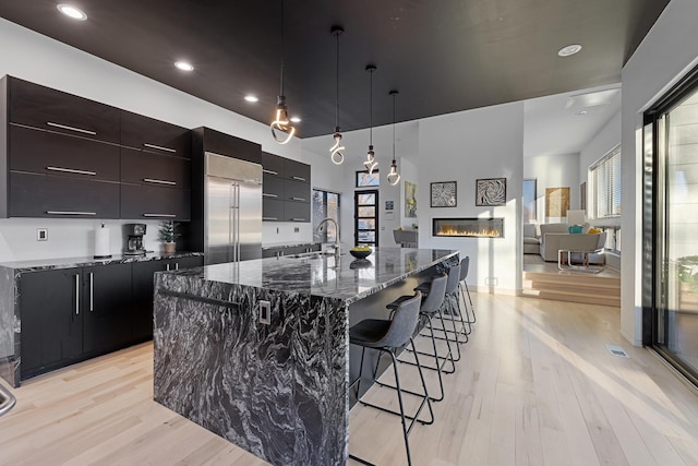 kitchen featuring a breakfast bar, stainless steel built in fridge, a sink, a glass covered fireplace, and modern cabinets