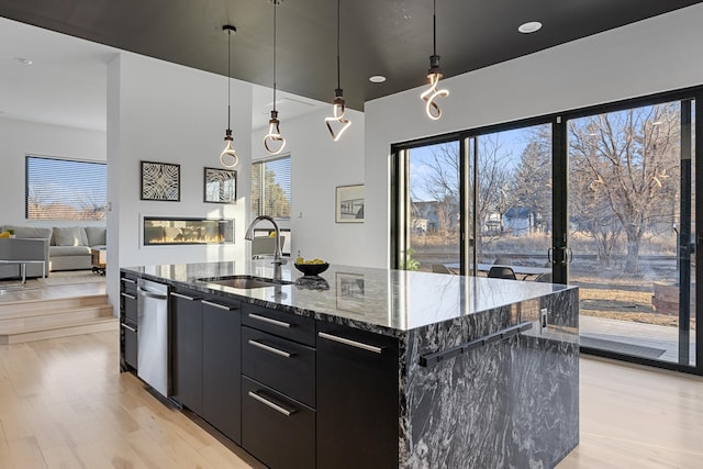 kitchen featuring a center island with sink, a sink, a glass covered fireplace, modern cabinets, and dark cabinets