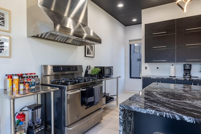 kitchen with dark cabinetry, dark stone counters, appliances with stainless steel finishes, wall chimney range hood, and modern cabinets