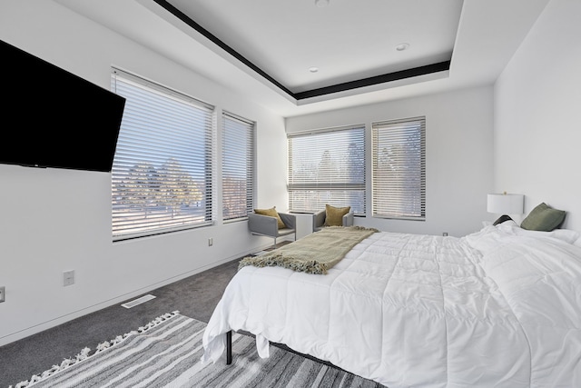 carpeted bedroom with a tray ceiling, baseboards, and visible vents