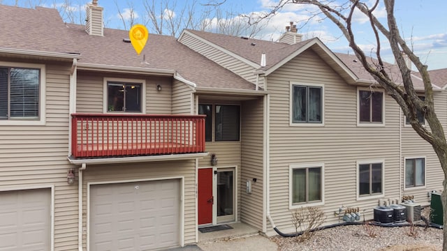 back of property featuring roof with shingles, a garage, a balcony, central AC unit, and a chimney