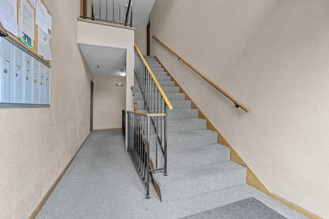 staircase featuring mail area, a textured wall, and baseboards