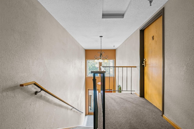 stairway featuring a notable chandelier, a textured wall, carpet floors, and a textured ceiling