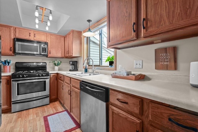 kitchen with light countertops, light wood-style flooring, stainless steel appliances, a raised ceiling, and a sink