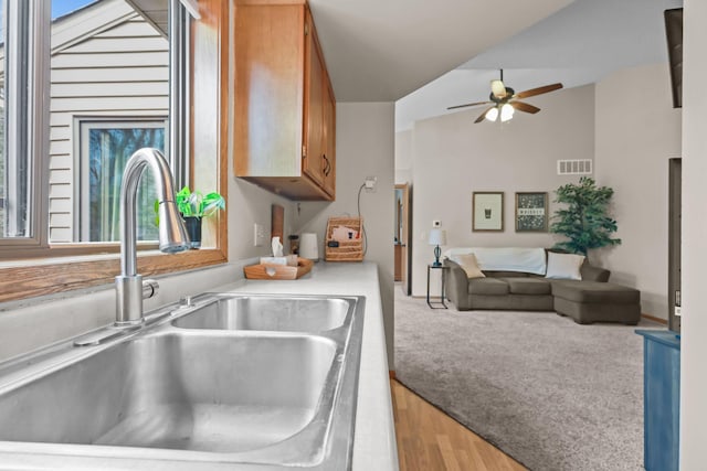 kitchen with brown cabinetry, visible vents, a sink, light countertops, and open floor plan