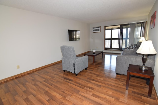 living area featuring a textured ceiling, a wall mounted air conditioner, baseboards, and wood finished floors