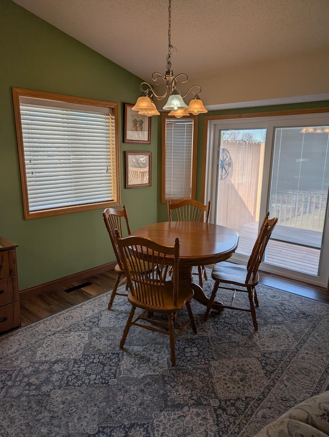 dining area with a textured ceiling, wood finished floors, baseboards, lofted ceiling, and a chandelier