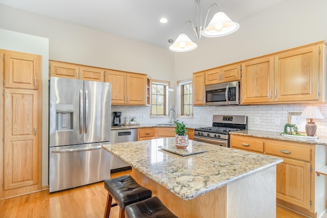 kitchen with a sink, a center island, stainless steel appliances, light wood finished floors, and light stone countertops