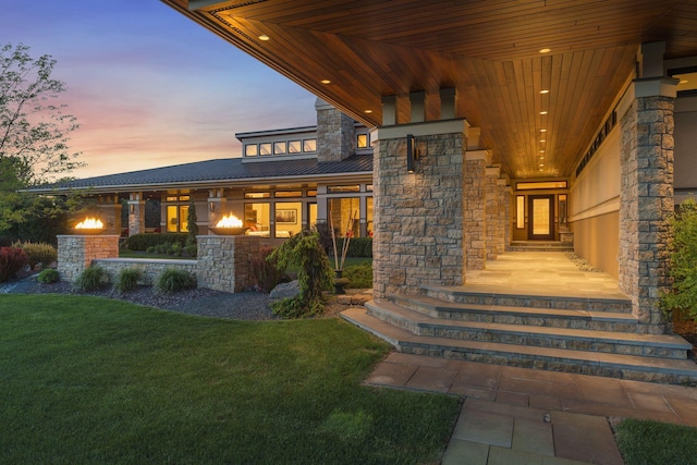 entrance to property with metal roof, stone siding, a lawn, and a standing seam roof