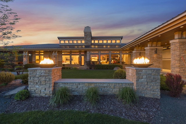 back of property at dusk featuring metal roof, stone siding, a lawn, and a standing seam roof