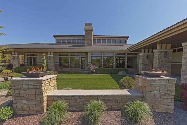 rear view of house featuring a chimney, a lawn, metal roof, and a standing seam roof