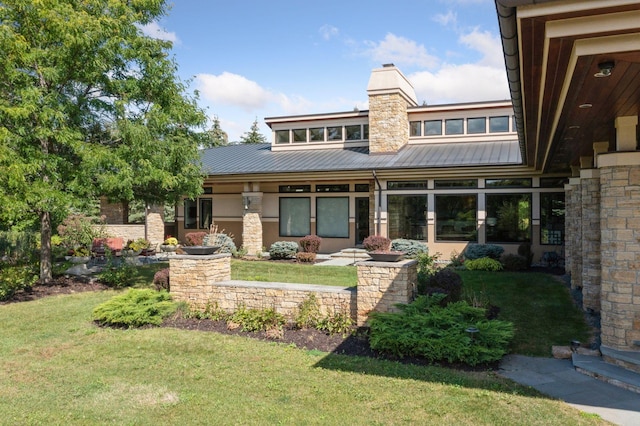 rear view of house with metal roof, a lawn, and a chimney