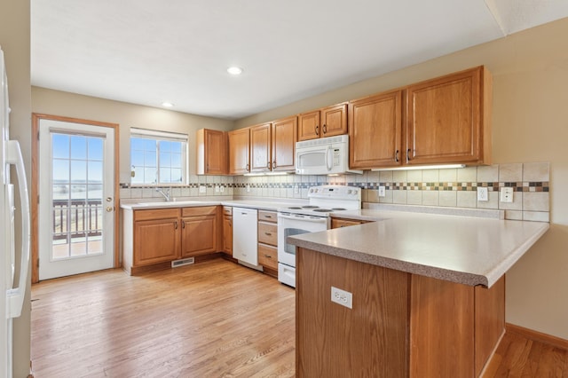 kitchen featuring visible vents, a sink, white appliances, a peninsula, and light wood finished floors