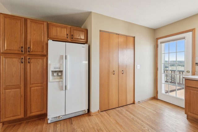 kitchen with brown cabinetry, baseboards, light countertops, light wood-style floors, and white fridge with ice dispenser