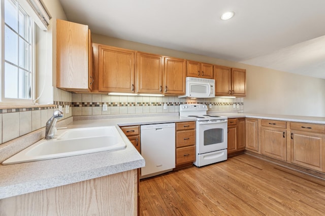 kitchen with light wood finished floors, tasteful backsplash, light countertops, white appliances, and a sink