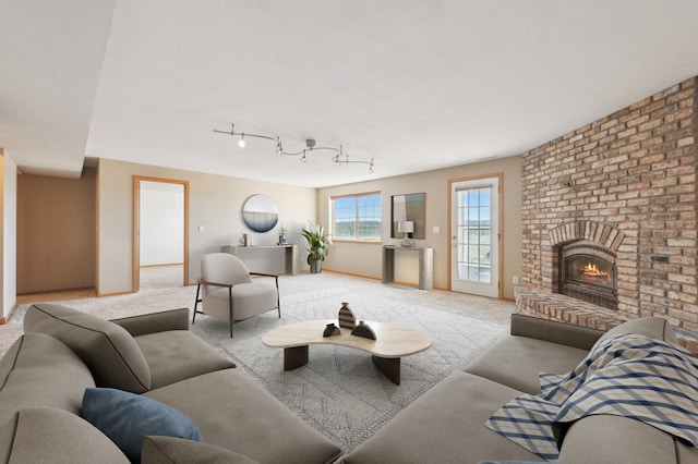 living area with baseboards, light carpet, a brick fireplace, and rail lighting