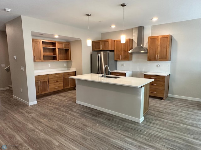 kitchen with brown cabinetry, dark wood finished floors, freestanding refrigerator, a sink, and wall chimney range hood