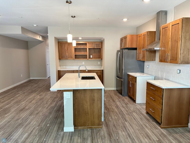 kitchen featuring wood finished floors, brown cabinetry, a sink, wall chimney exhaust hood, and tasteful backsplash