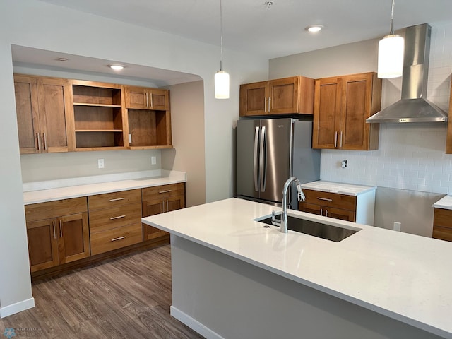 kitchen with dark wood-style floors, freestanding refrigerator, a sink, wall chimney exhaust hood, and brown cabinets