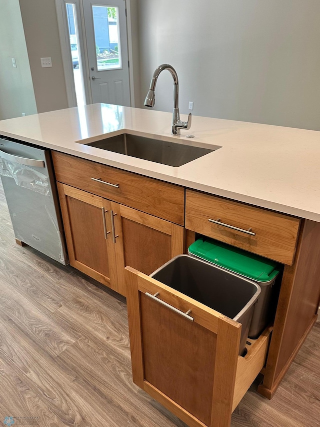 kitchen with brown cabinets, light wood finished floors, a sink, stainless steel dishwasher, and light countertops