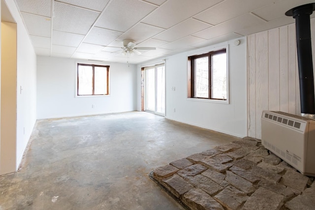 empty room with heating unit, a healthy amount of sunlight, concrete flooring, and a ceiling fan