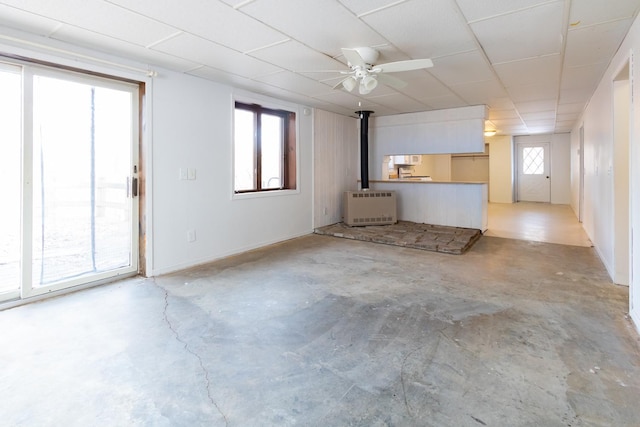 unfurnished living room featuring a wood stove, heating unit, a ceiling fan, and concrete floors