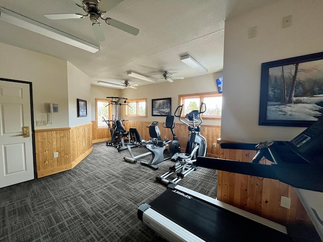 gym with dark carpet, wooden walls, a textured ceiling, wainscoting, and ceiling fan