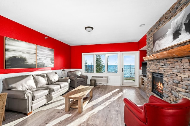 living area with a wall unit AC, a fireplace, and wood finished floors