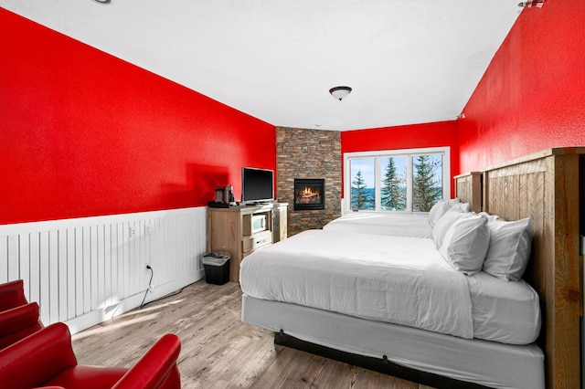bedroom featuring a textured wall, a wainscoted wall, a fireplace, and wood finished floors