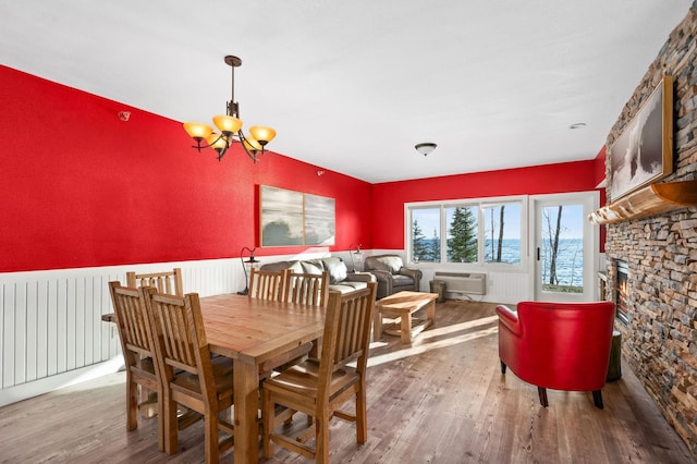 dining area featuring a wall mounted AC, a wainscoted wall, a fireplace, wood finished floors, and an inviting chandelier