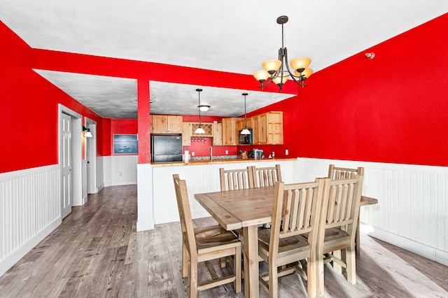 dining area with wood finished floors, a chandelier, and wainscoting