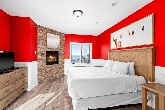 bedroom with a stone fireplace, wainscoting, and wood finished floors